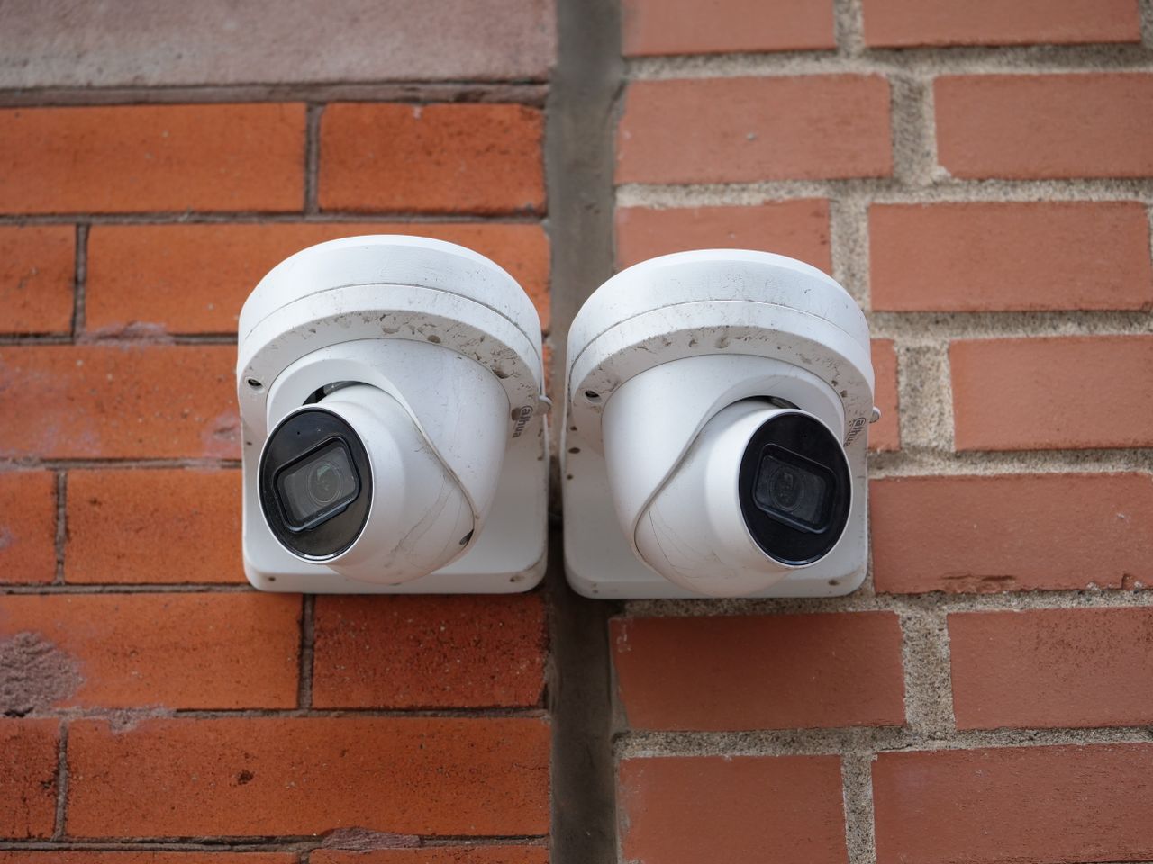 home-bg-img Two white dome security cameras mounted on a brick wall for urban surveillance.
