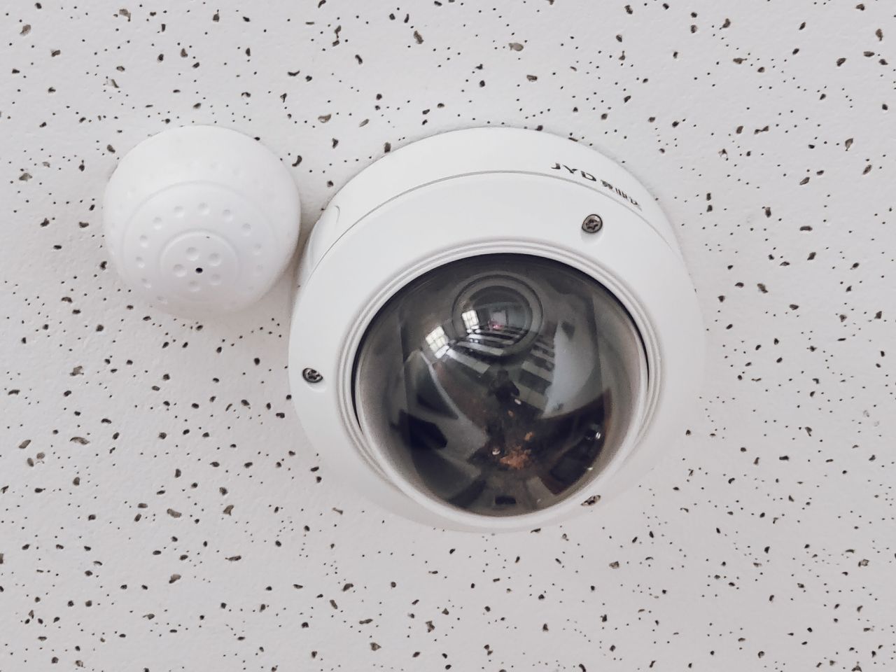product-01 Close-up of a round dome surveillance camera installed on a speckled ceiling for security monitoring.